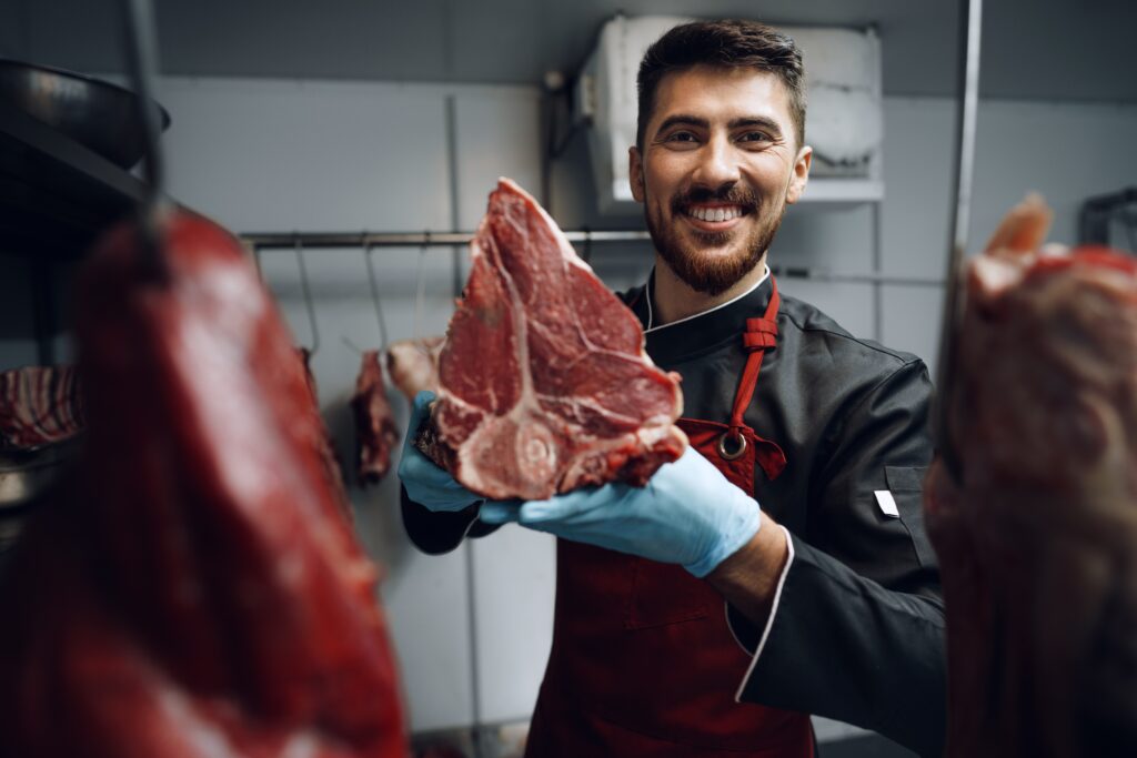 Young,Butcher,Holding,Raw,Meat,Steaks,In,Fridge,Of,Grocery